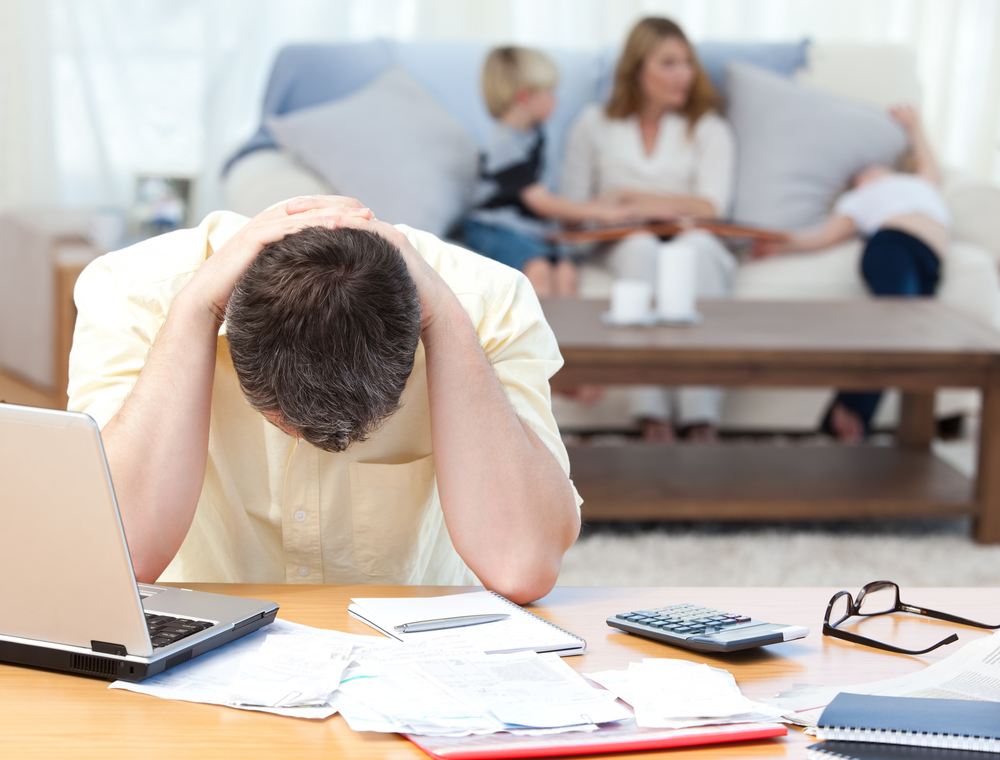 Man calculating his credit card bills while his family is on the sofa