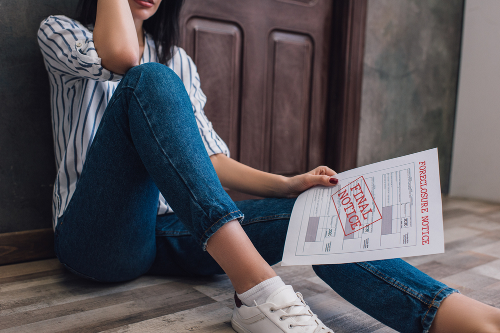 Woman sitting on the floor holding "final notice" of foreclosure